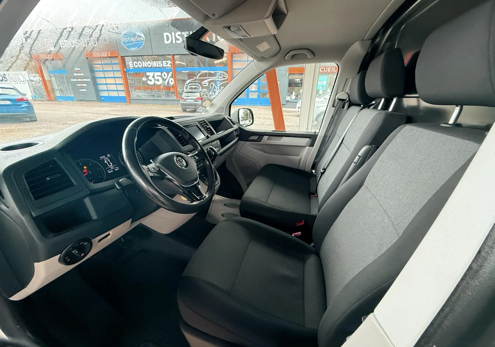 Intérieur du Volkswagen Transporter L1H1 2018 vu côté conducteur, sièges tissu gris et tableau de bord noir.