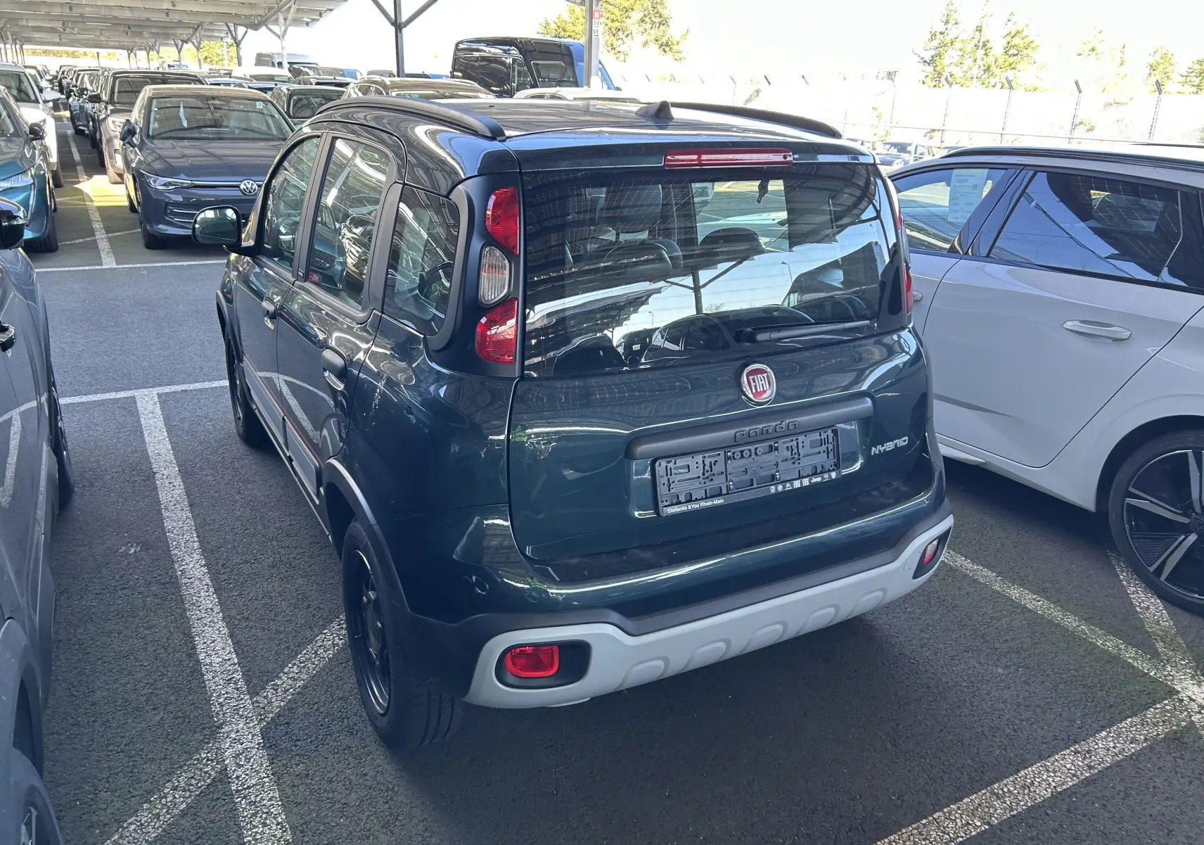 Vue 3/4 arrière d'une FIAT Panda City Cross gris minuit avec badge Hybrid, stationnée entre deux véhicules.