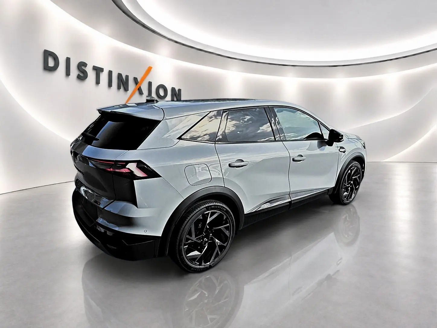 Renault Symbioz gris cassiope en 3/4 arrière droit, avec jantes noires et vitres arrière surteintées dans un showroom lumineux.