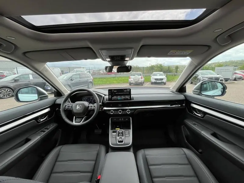 Vue intérieure avant du Honda CR-V 2024 avec tableau de bord noir, volant cuir multifonction et toit panoramique en verre.