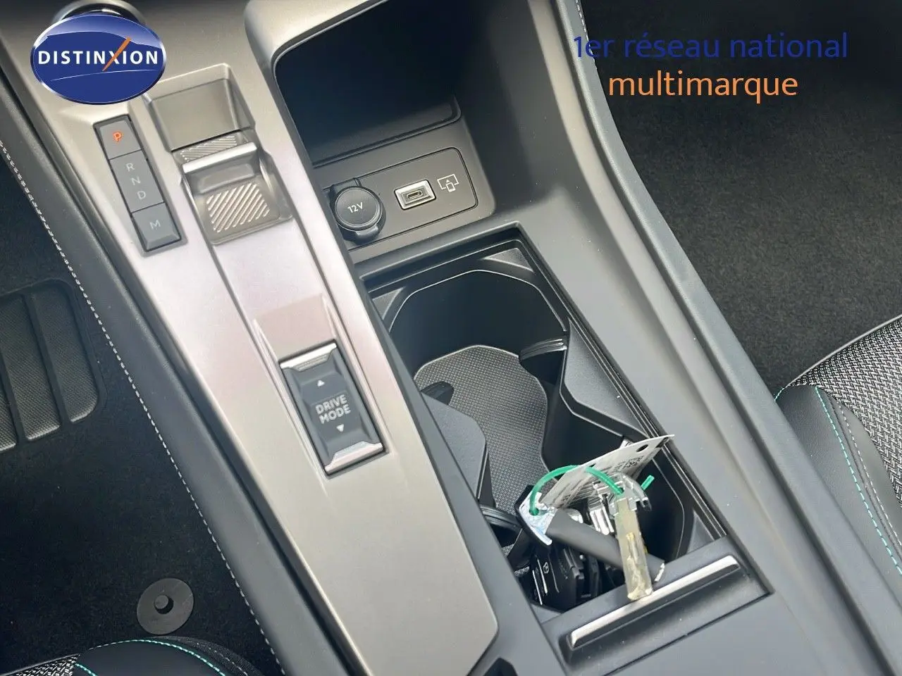 Gros plan sur la console centrale de la Peugeot 308 hybride 2024, avec levier de vitesses et porte-gobelets noir.