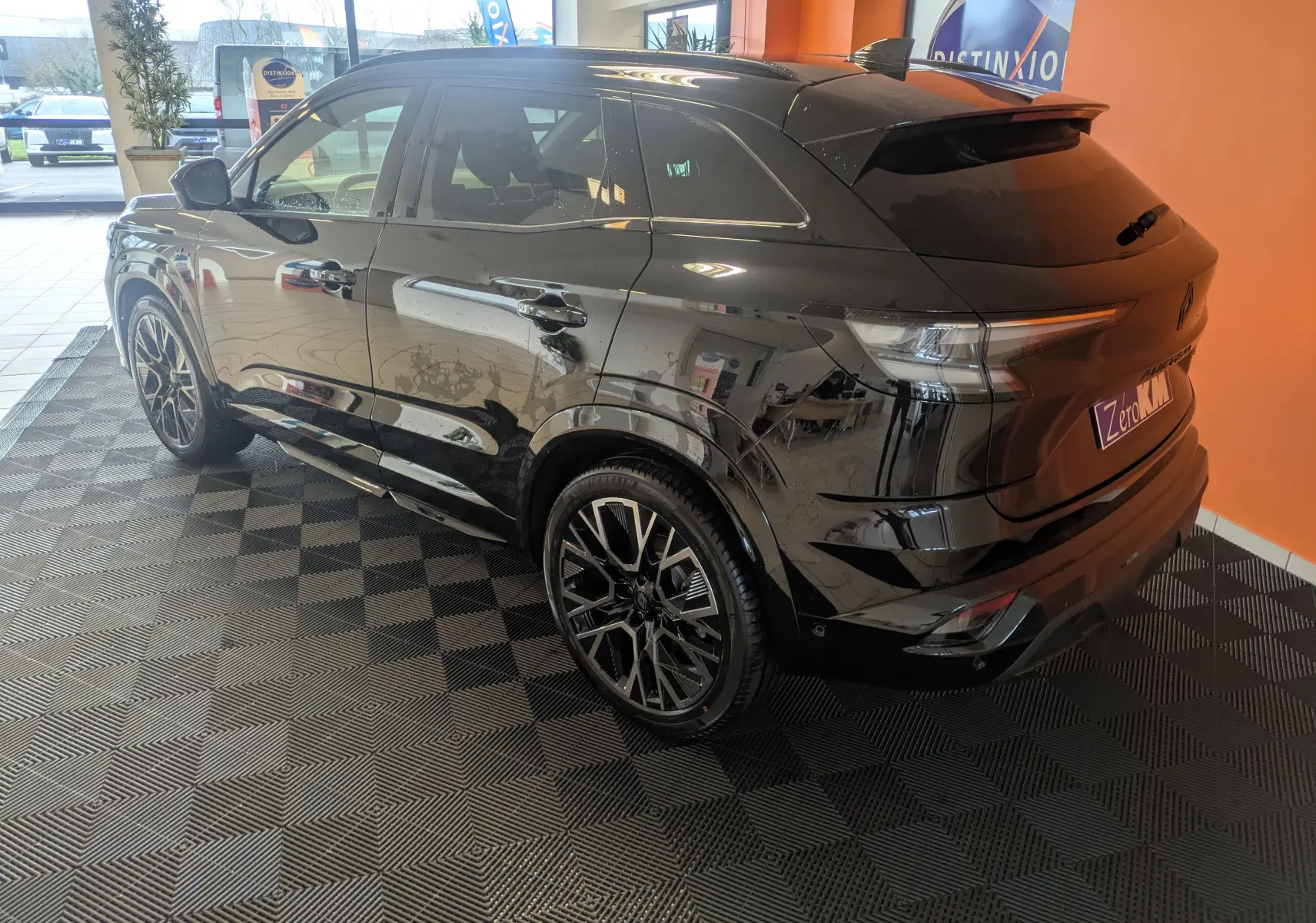 Renault Austral noir en 3/4 arrière droit, jantes alliage noires, intérieur showroom avec mur orange en arrière-plan.