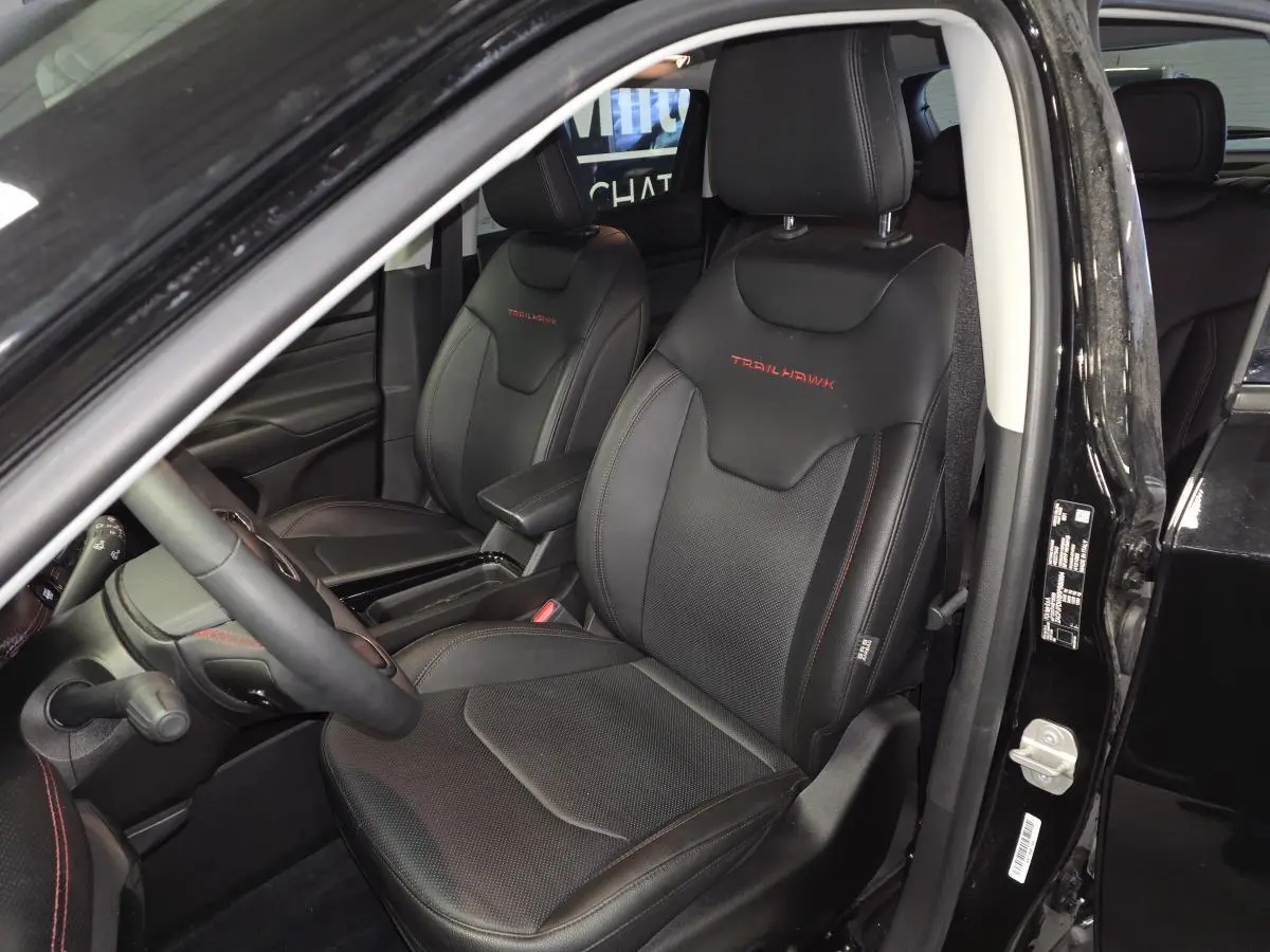 Intérieur avant du Jeep Compass Trailhawk 2024 noir, sièges cuir noirs avec logo Trailhawk rouge visible sur les appuie-têtes.