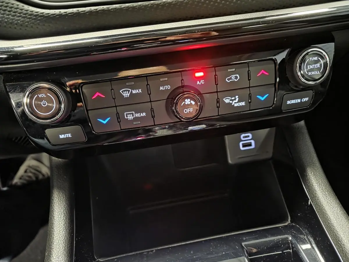 Tableau de bord noir du Jeep Compass 2024 avec commandes climatisation et réglages audio éclairés en rouge et bleu