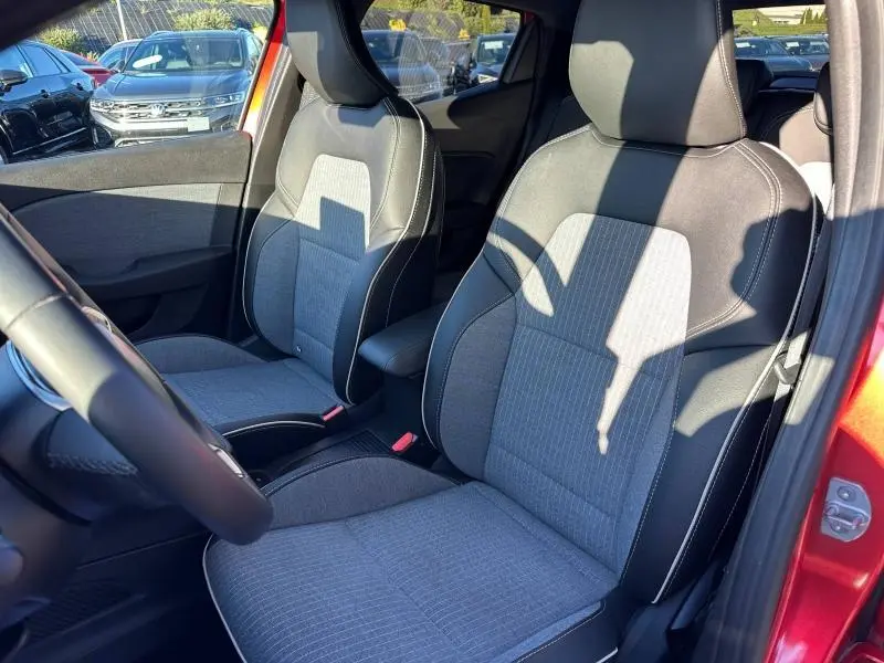 Vue intérieure côté avant droit de la Renault Clio 1.6 E-Tech rouge Flamme, sièges tissu gris avec surpiqûres blanches.