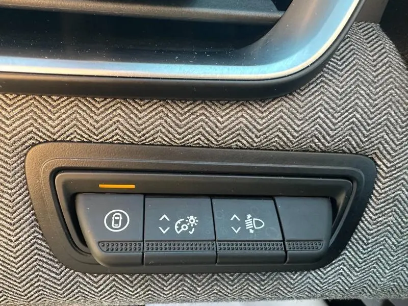 Gros plan sur les commandes d’éclairage et de verrouillage, intégrées dans un habillage tissu à chevrons de la Renault Clio Rouge Flamme 2025.