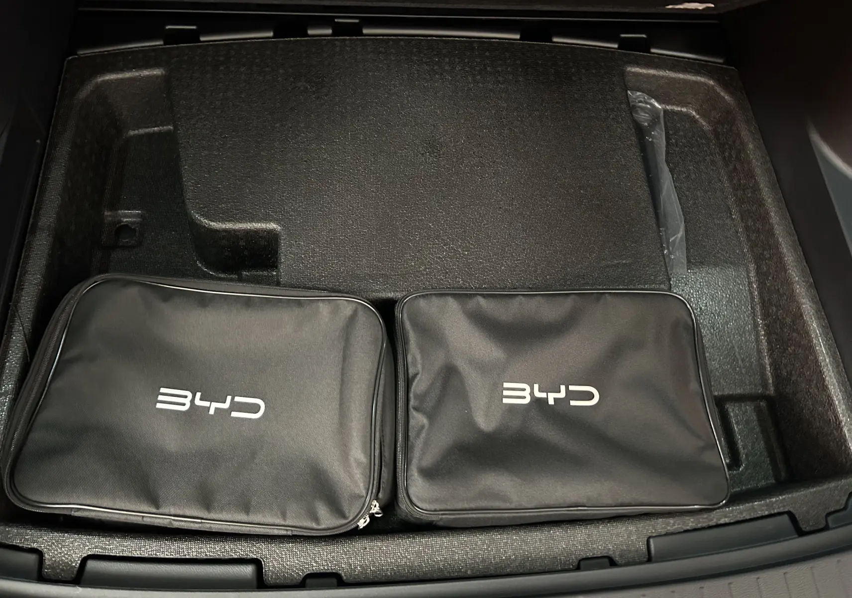 Vue plongeante sur le coffre avec deux trousses noires BYD posées dans un compartiment en mousse noire.