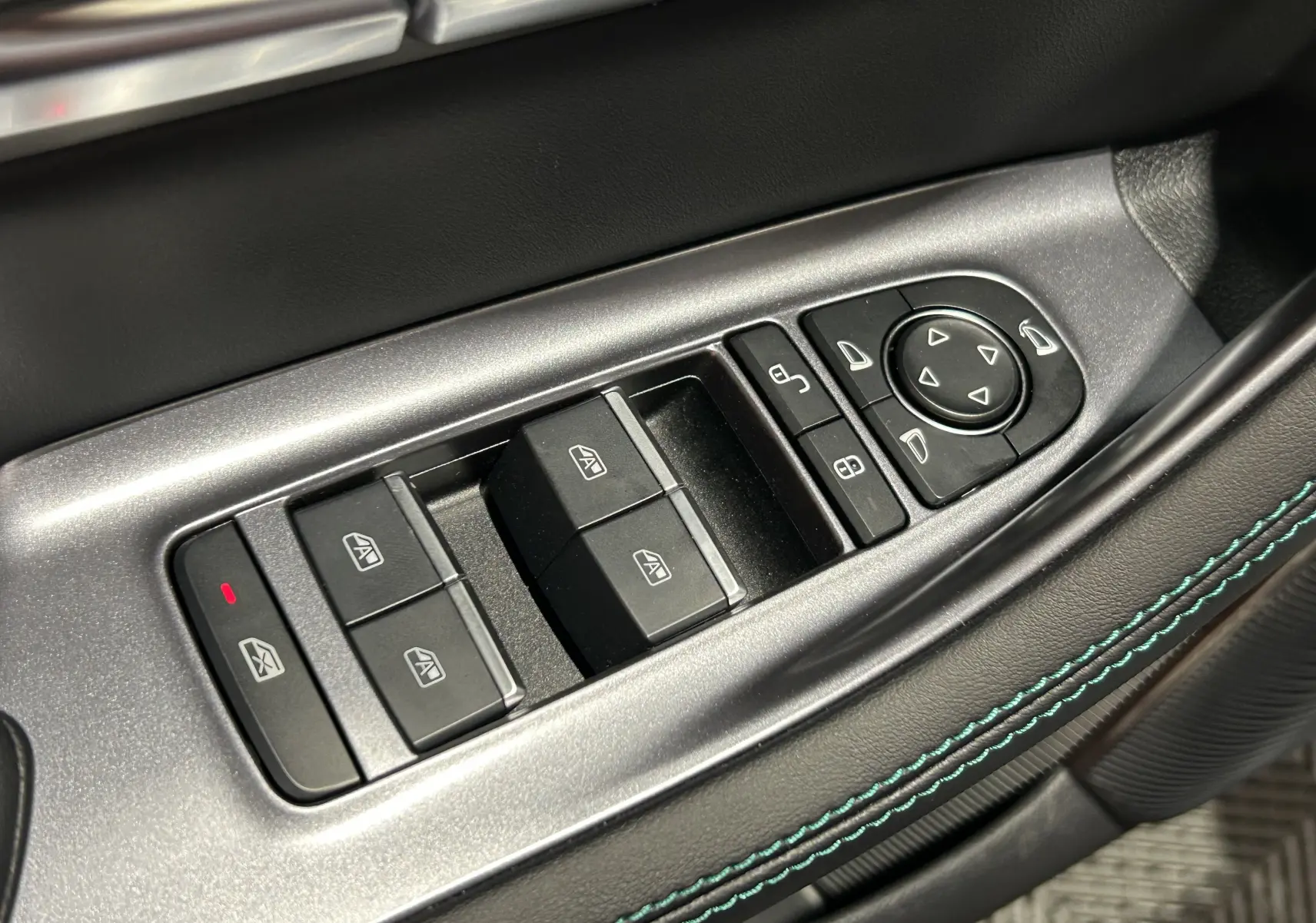 Gros plan sur les commandes de lève-vitres et rétroviseurs côté gauche avec surpiqûres bleu-vert sur cuir noir.