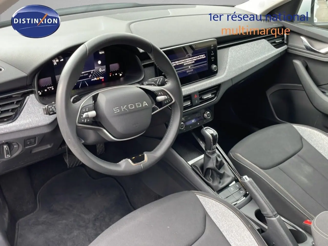 Vue intérieure du poste de conduite du Skoda Kamiq blanc glacier 2025, avec volant multifonction et écran tactile central.