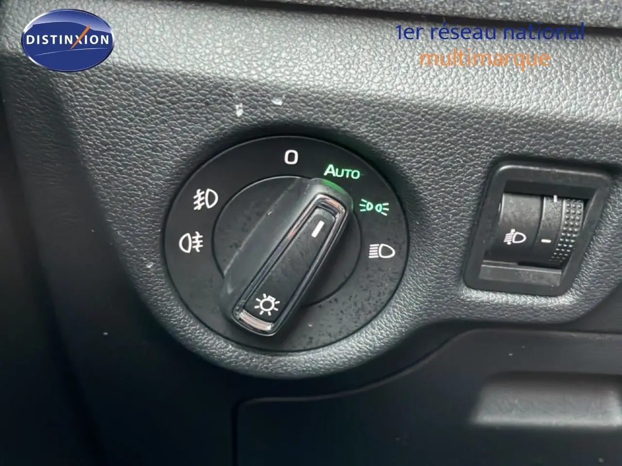 Gros plan sur le bouton de commande des phares du Skoda Kamiq blanc glacier, avec réglage automatique activé.
