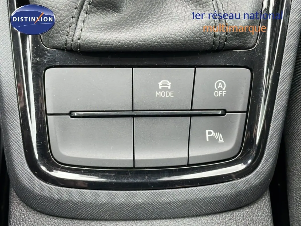 Gros plan sur les commandes de mode de conduite et assistance au stationnement dans l’habitacle du Skoda Kamiq blanc glacier 2025.