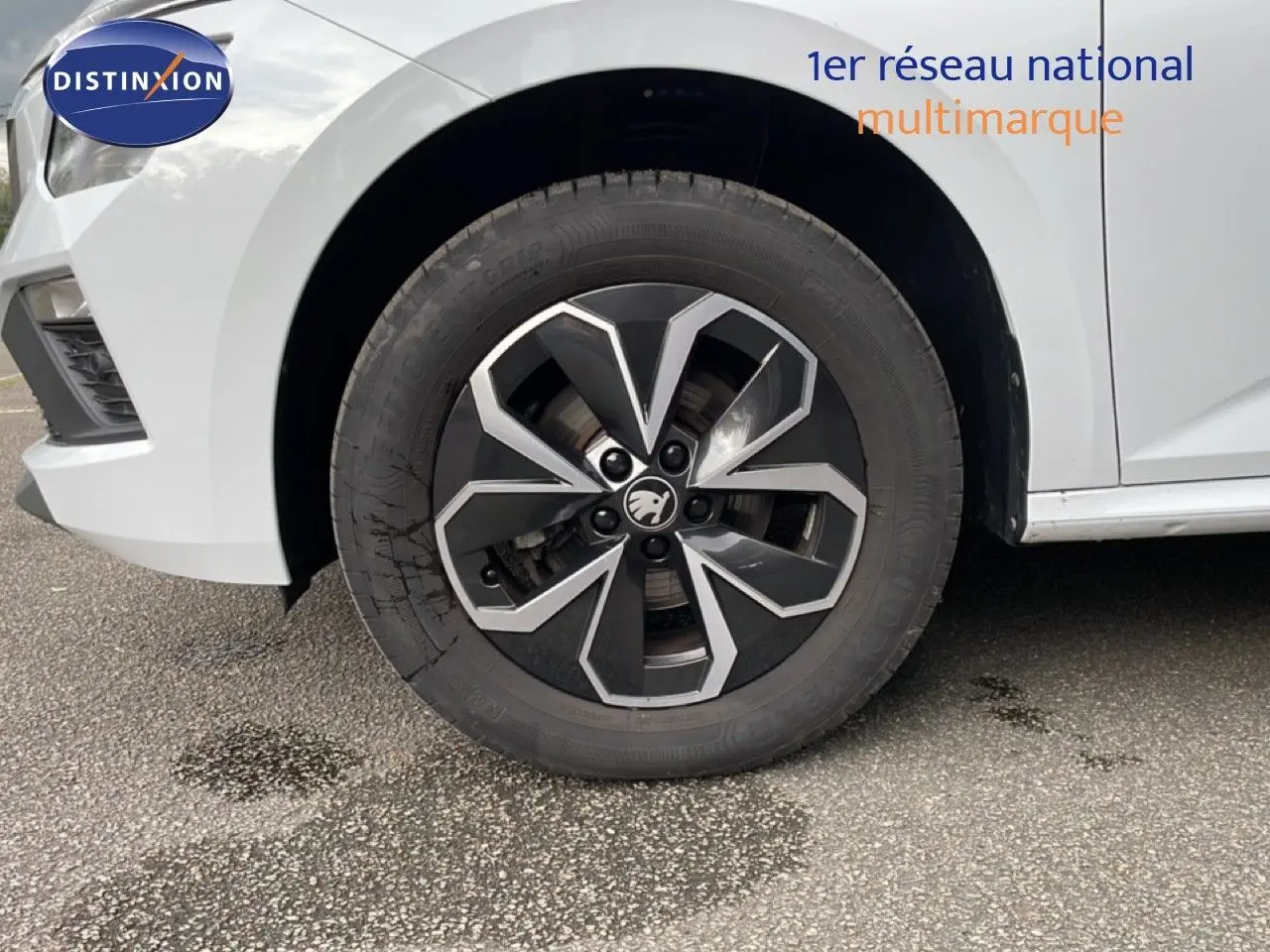 Gros plan sur la roue avant gauche d'un Skoda Kamiq blanc glacier avec jante noire et argentée au design moderne.