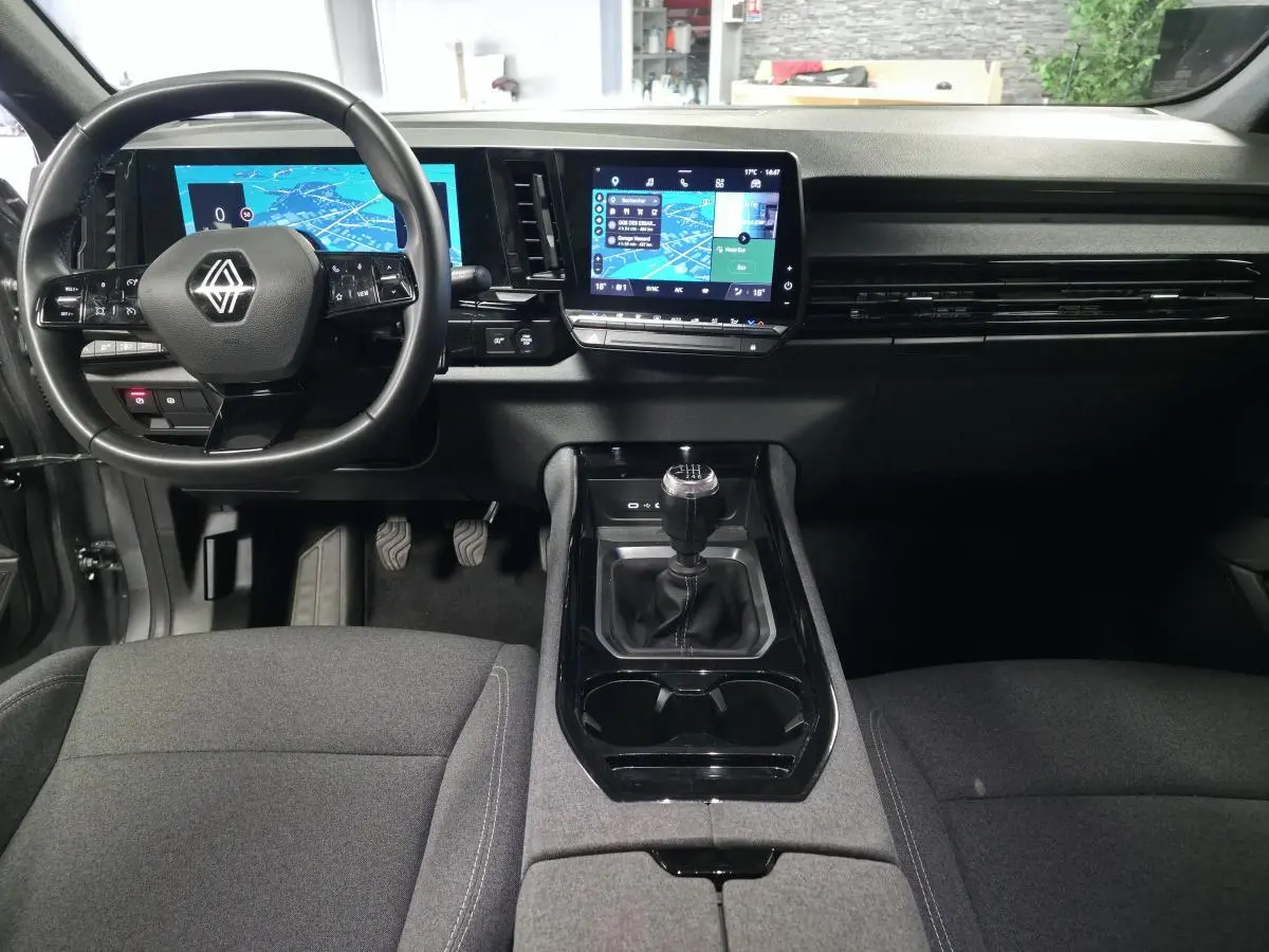 Vue intérieure avant du Renault Austral gris, mettant en valeur le volant multifonction, l'écran tactile central et la boîte manuelle.