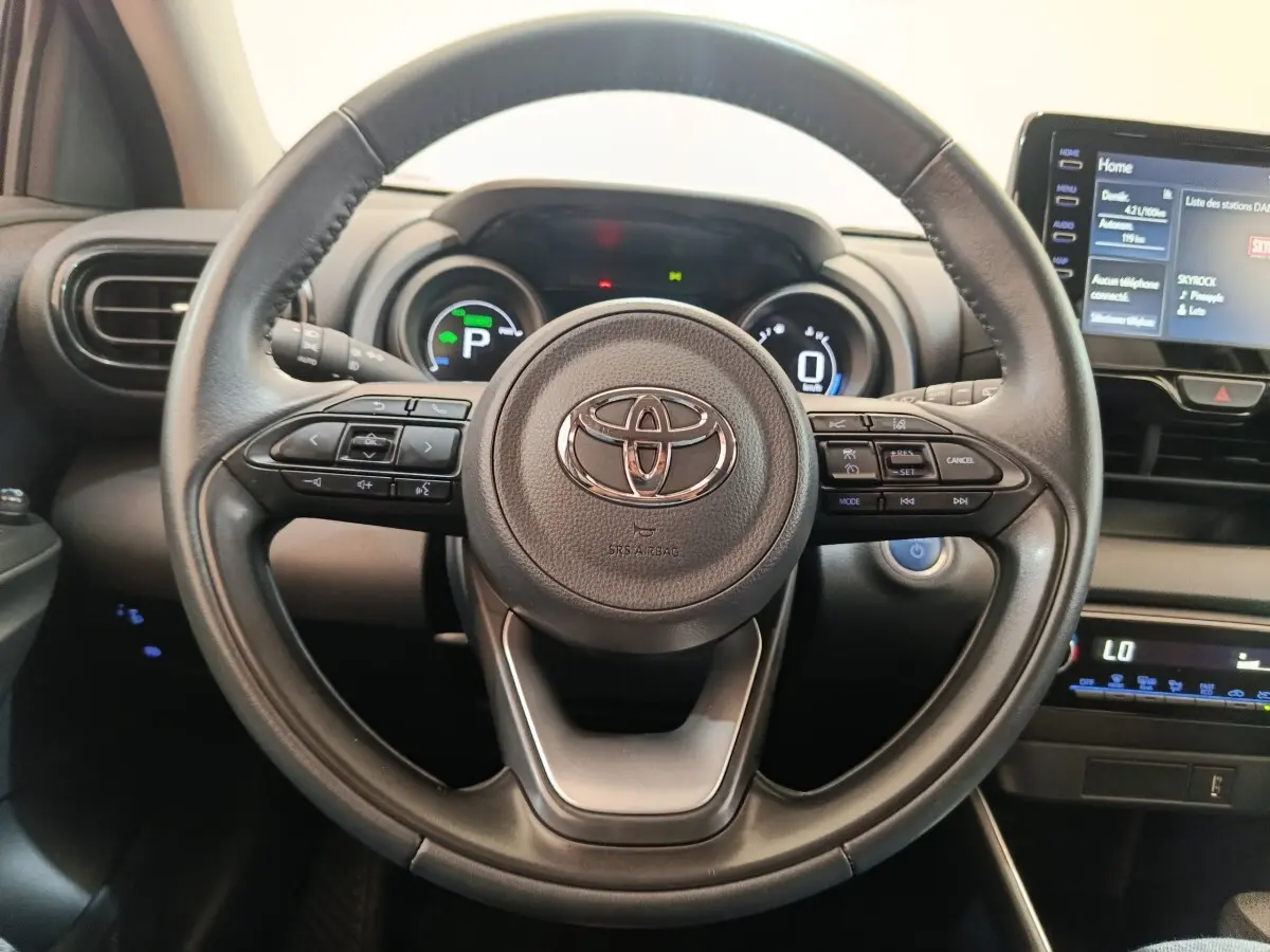 Vue rapprochée du volant cuir multifonctions noir de la Toyota Yaris Hybride 116h avec tableau de bord digital et écran tactile.