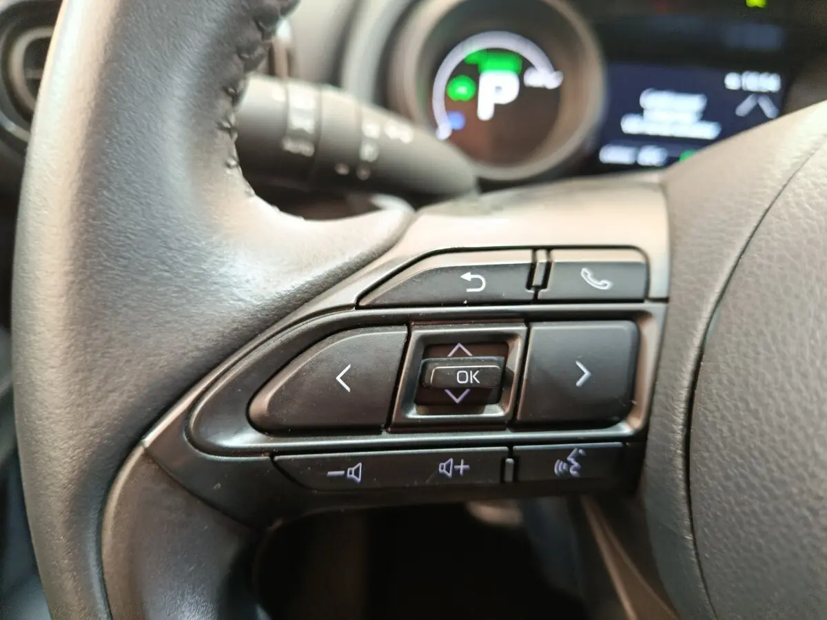 Gros plan sur les commandes multifonctions noires du volant cuir de la Toyota Yaris Hybride 116h 2023.
