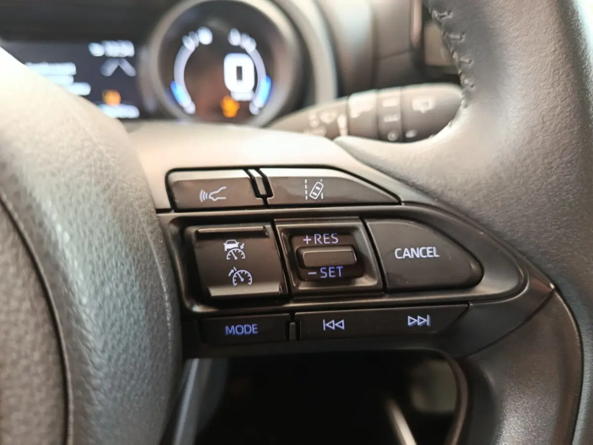 Gros plan sur les commandes du volant cuir à droite de la Toyota Yaris hybride gris clair 2023, affichage digital en arrière-plan.