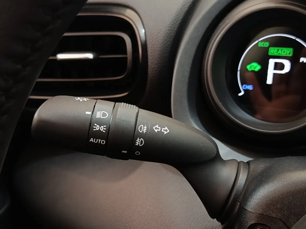 Gros plan sur la commande des phares et clignotants à gauche du volant dans l’habitacle noir de la Toyota Yaris hybride 2023.