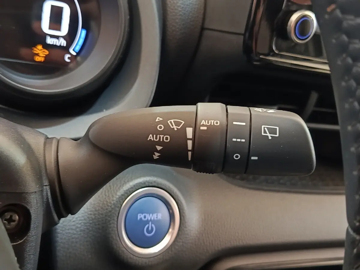 Gros plan sur la commande d’essuie-glace automatique et bouton Power bleu du tableau de bord d’une Toyota Yaris hybride gris clair 2023.