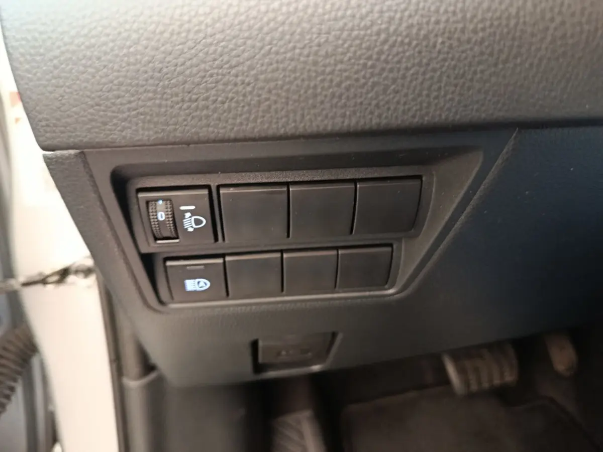 Gros plan sur les commandes de réglage des phares à gauche sous le tableau de bord d'une Toyota Yaris hybride gris clair 2023.