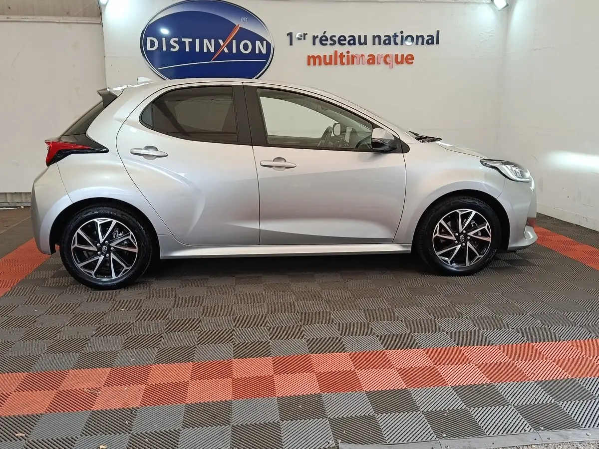 Vue latérale droite d'une Toyota Yaris Hybride 116h Design gris clair, avec jantes alliage et feux arrière distinctifs.