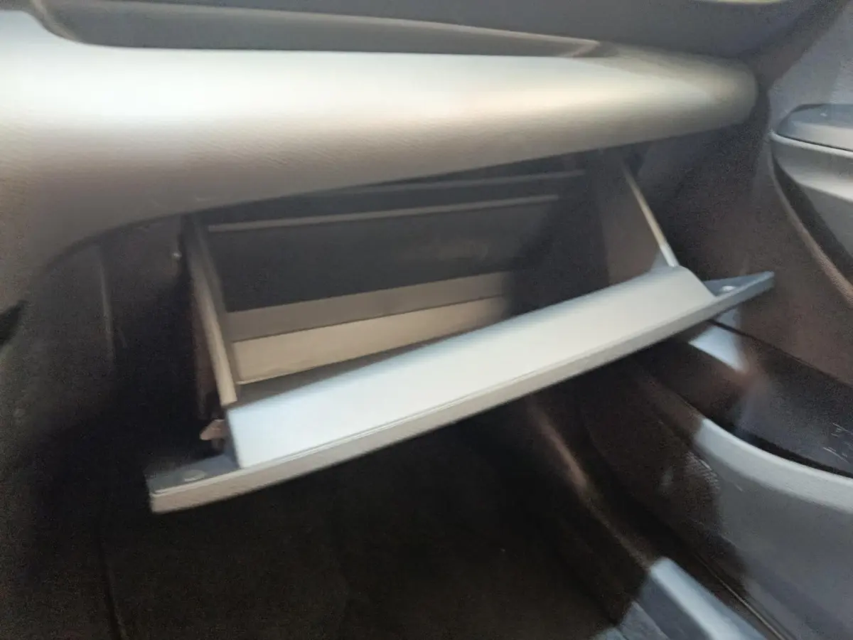 Gant de boîte à gants ouvert côté passager dans l'habitacle sombre d'une Toyota Yaris Hybride 116h Design 2023.