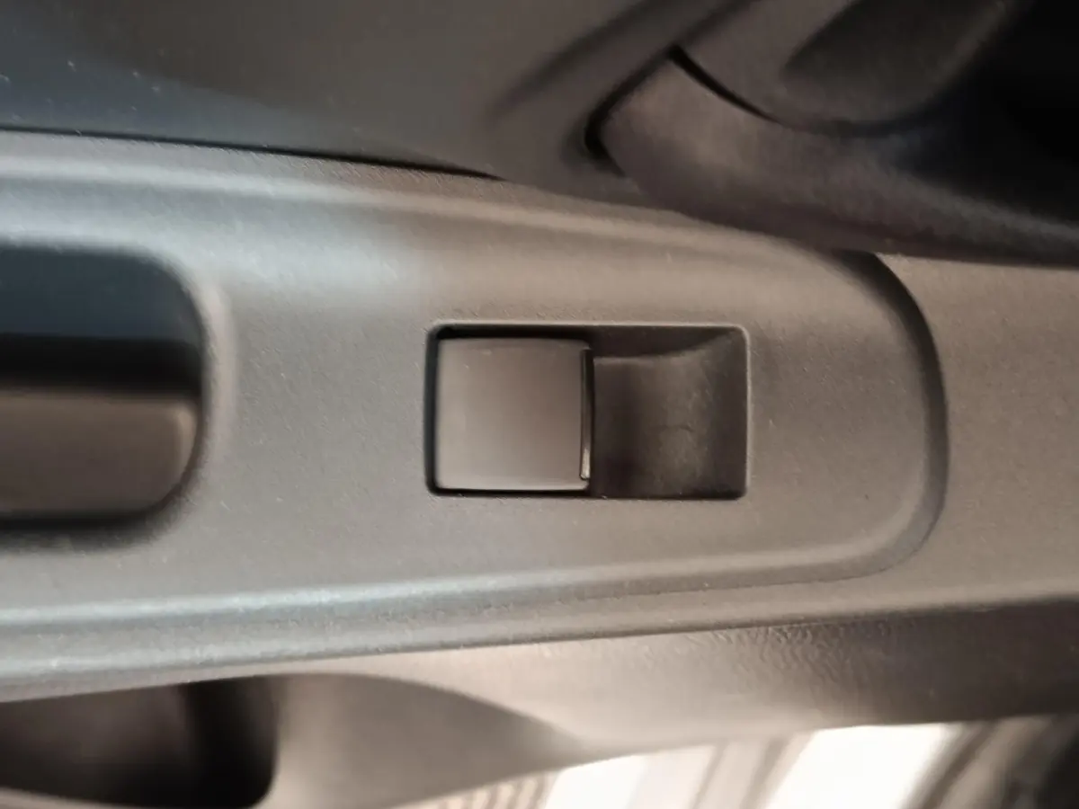 Gros plan sur le bouton de commande de la vitre côté conducteur dans l'habitacle gris foncé d'une Toyota Yaris Hybride 2023.