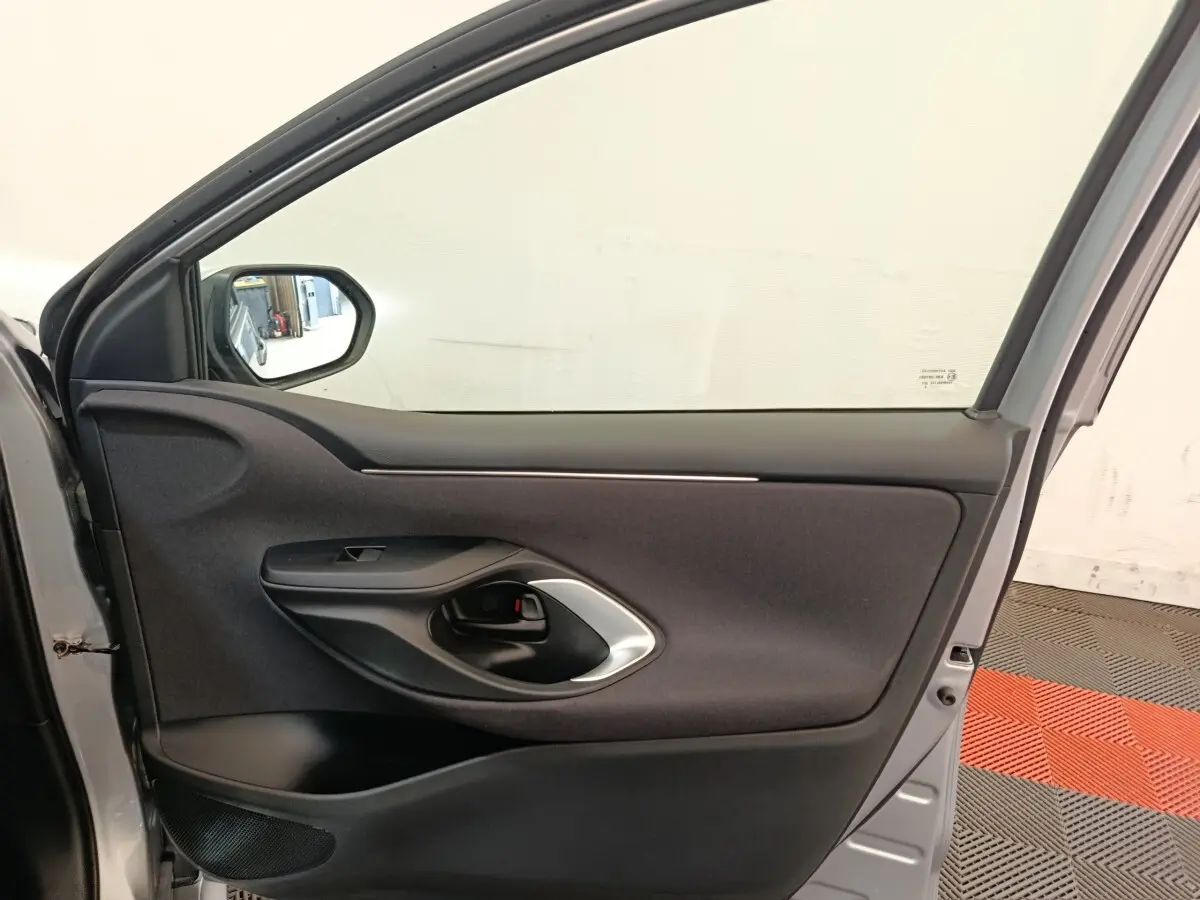 Vue intérieure de la porte avant gauche gris clair de la Toyota Yaris Hybride 116h Design 2023 avec poignée noire et garniture tissu.