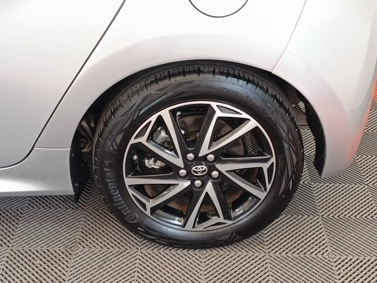 Gros plan sur la roue arrière droite gris clair de la Toyota Yaris Hybride 116h Design avec jante alliage noire et argent.