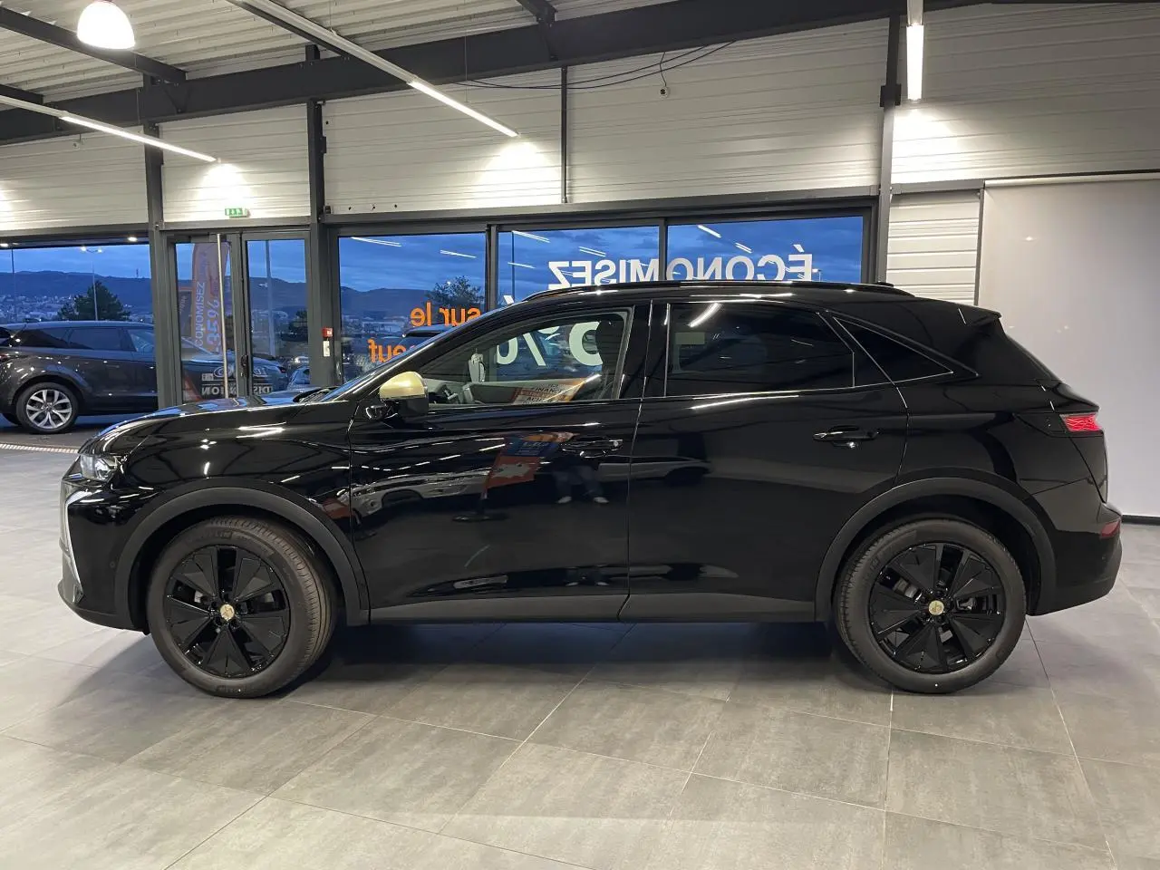 DS7 Crossback noir métallisé vu de profil côté gauche en intérieur avec jantes noires et coques de rétroviseurs dorées.