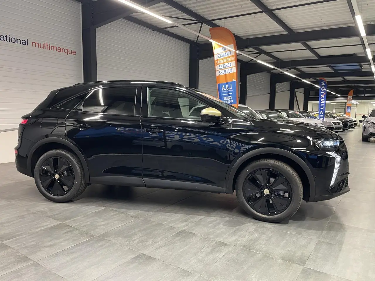 Vue latérale droite d'un DS7 Crossback noir métallisé avec jantes noires et coques de rétroviseurs dorées satinées en intérieur showroom.