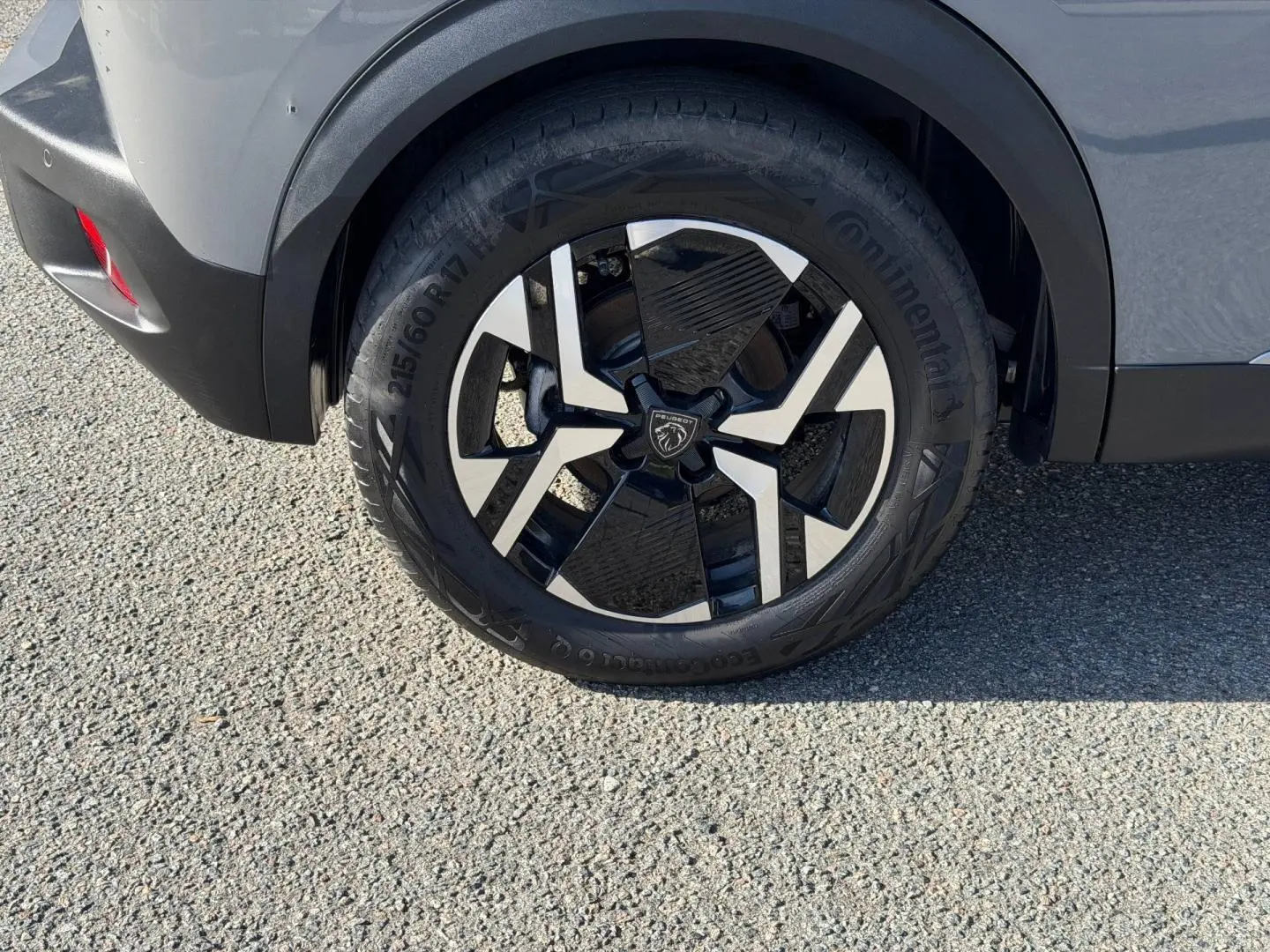 Gros plan sur la roue arrière droite du Peugeot e-2008 gris Artense avec jante alu noire et argentée.
