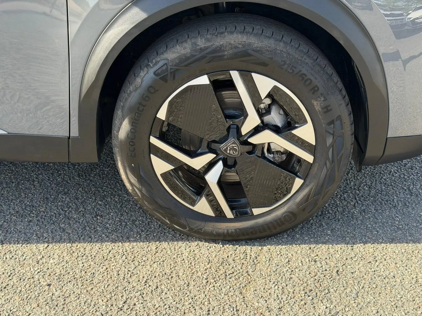 Gros plan sur la roue avant droite en jante alu bicolore du Peugeot e-2008 gris Artense, avec partie de la carrosserie visible.