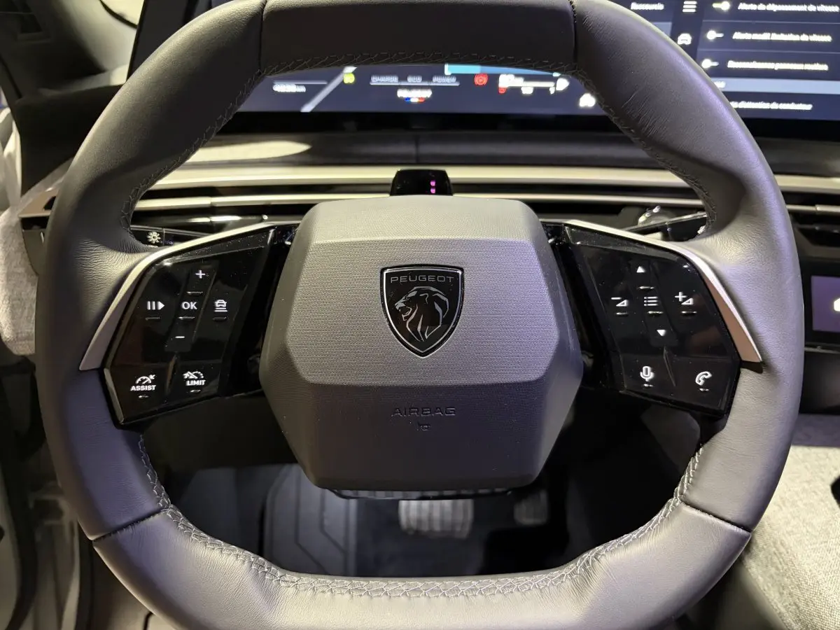 Volant cuir gris du Peugeot 3008 1.2 Hybrid 145 Allure, avec commandes multifonctions et logo lion central visible.