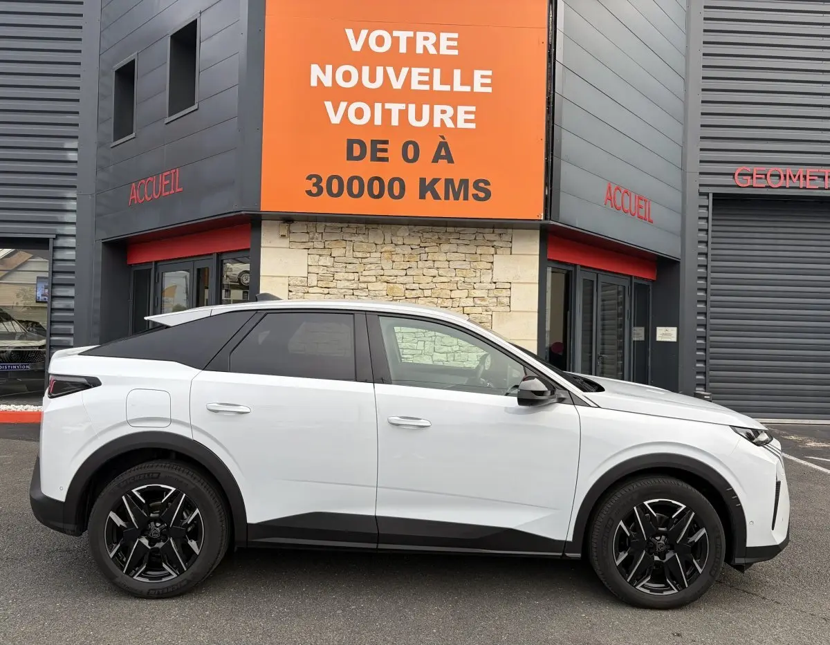 Vue latérale droite du Peugeot 3008 blanc 2026 avec toit noir et jantes noires devant un bâtiment commercial.