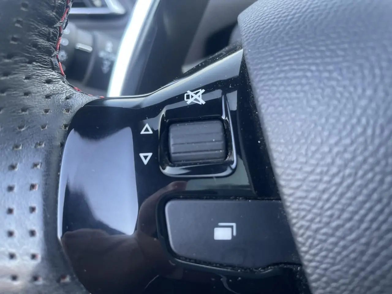 Gros plan sur les commandes noires du volant cuir perforé avec surpiqûres rouges d'une Peugeot 308 SW Bleu Vertigo.