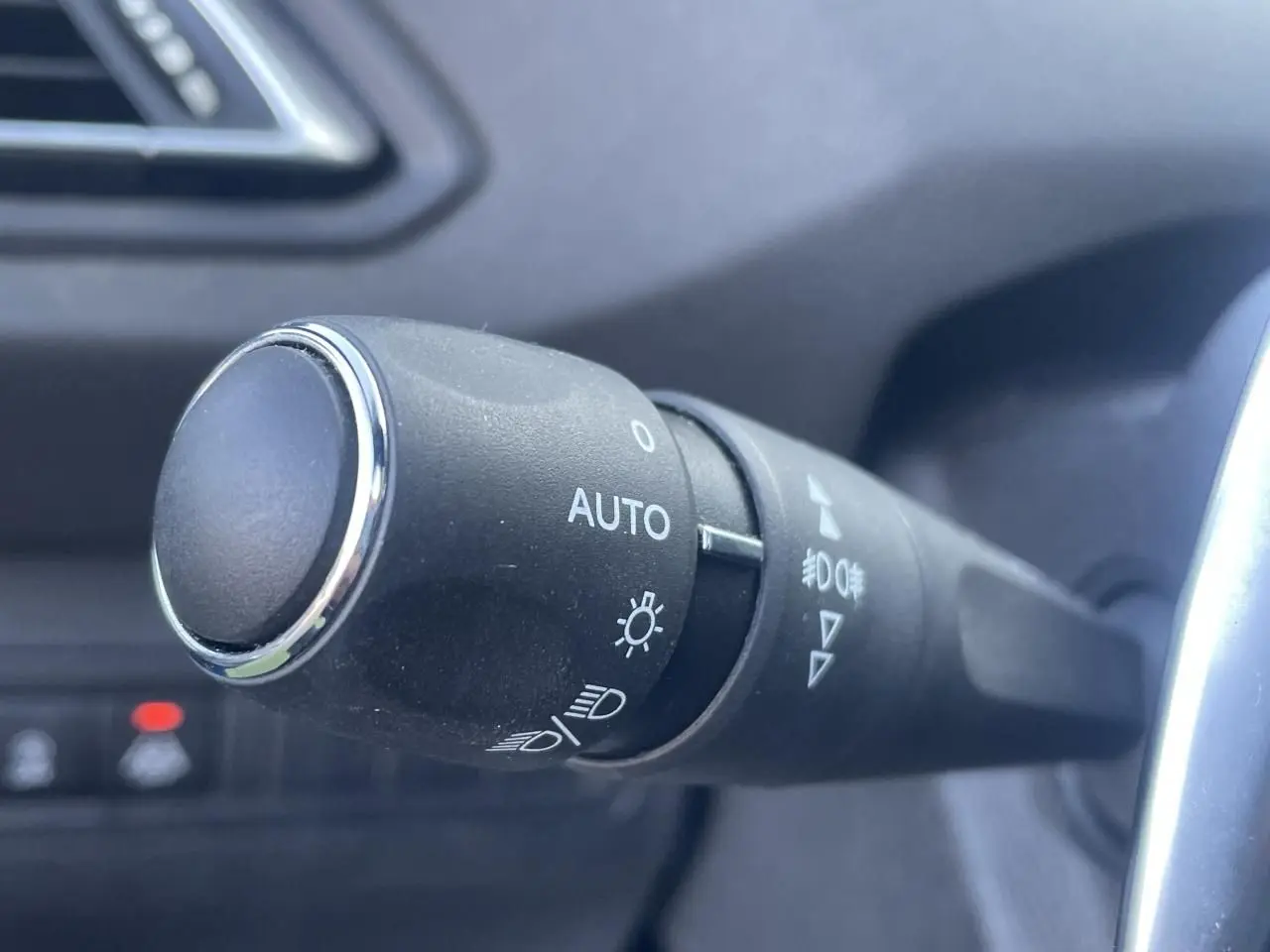 Gros plan sur la commande des feux automatique dans l'habitacle sombre d'une Peugeot 308 SW Bleu Vertigo 2021.