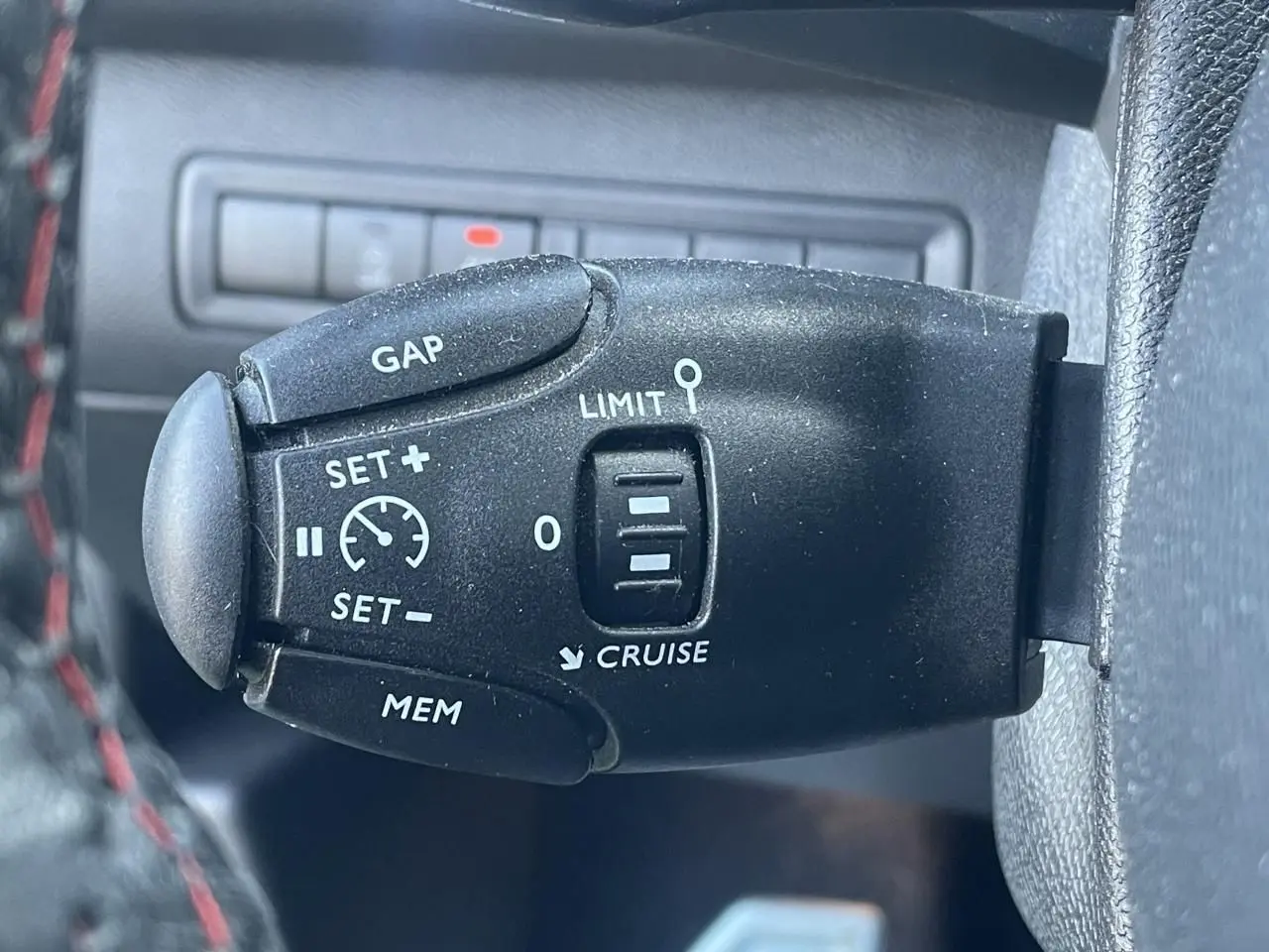 Gros plan sur la commande de régulateur de vitesse noire à gauche du volant d'une Peugeot 308 SW bleu Vertigo.