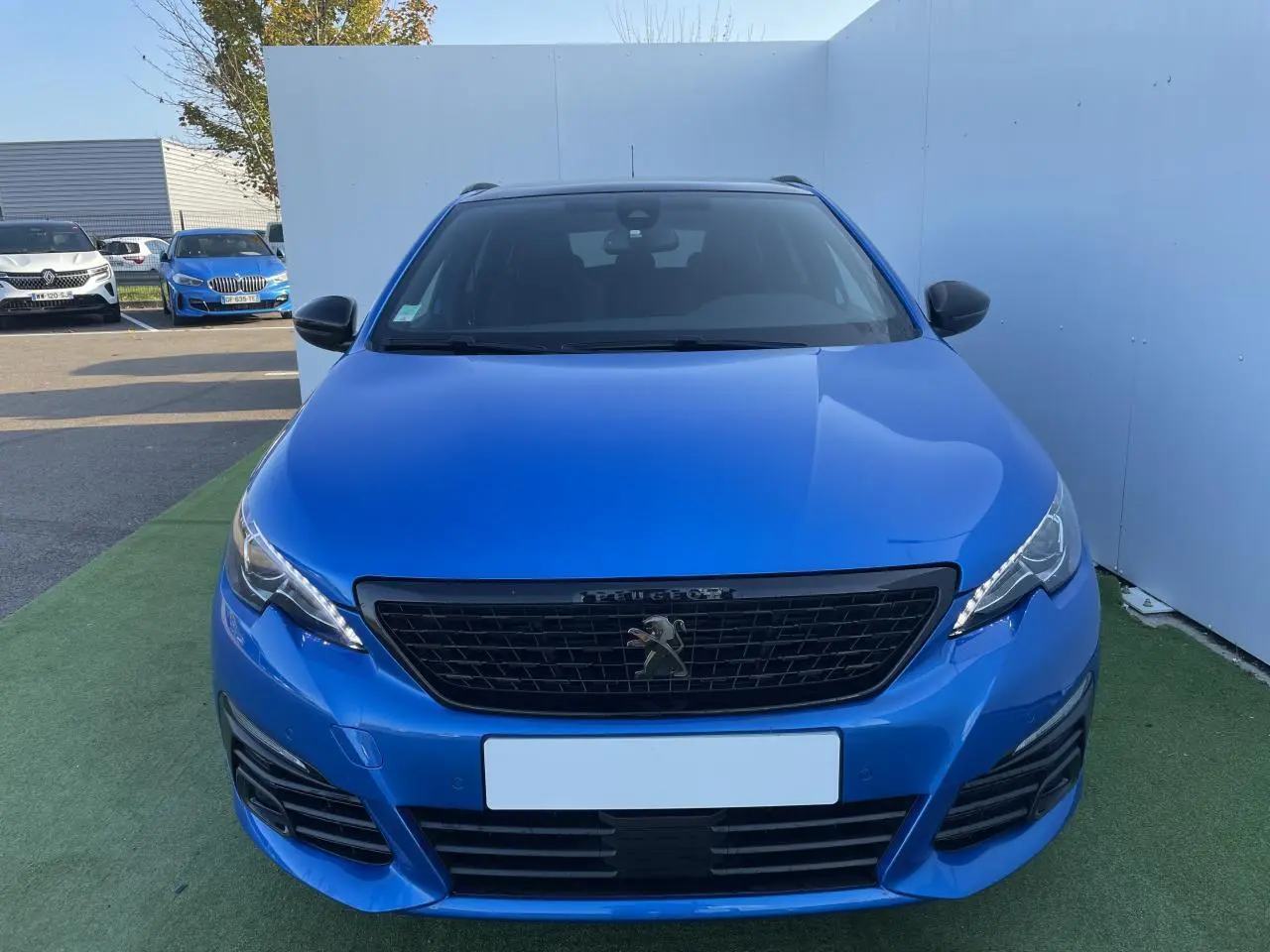 Vue frontale d'une Peugeot 308 SW 2 bleu Vertigo avec calandre noire et feux LED distinctifs.