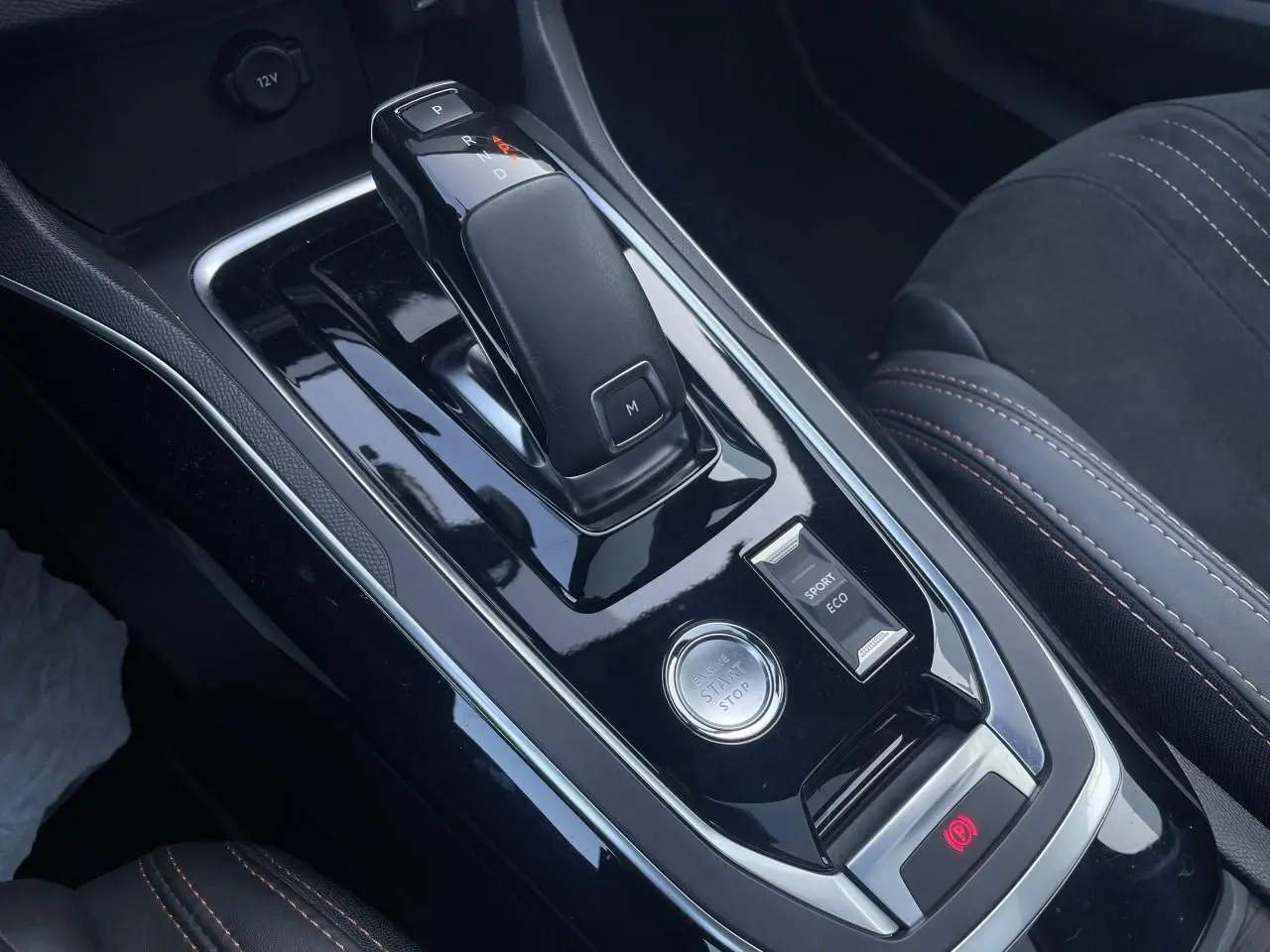 Gros plan sur la console centrale noire brillante de la Peugeot 308 SW 2021, avec levier de boîte auto et bouton start/stop.