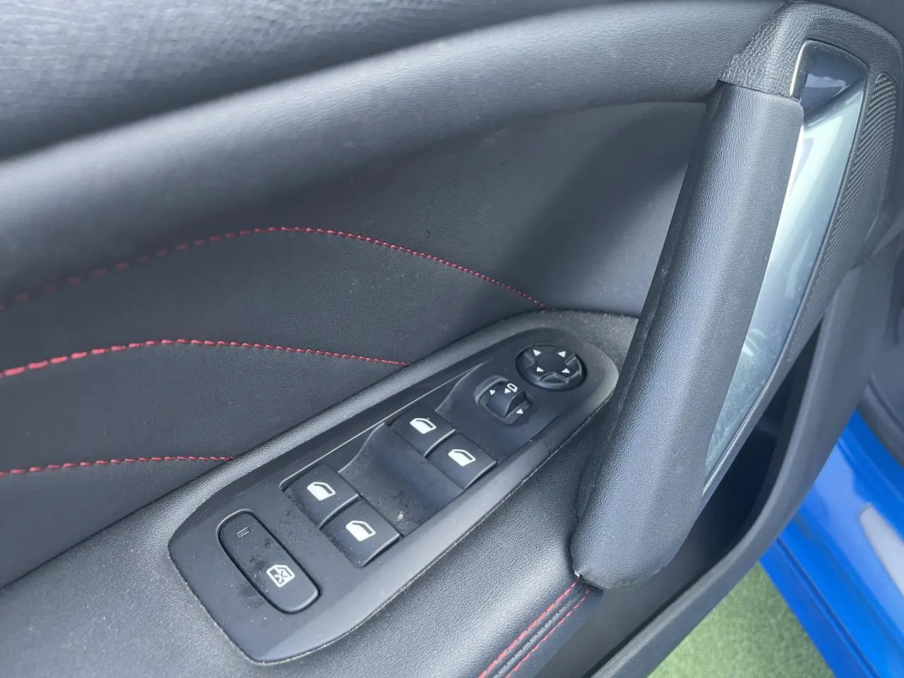 Gros plan sur la porte avant gauche d'une Peugeot 308 SW bleu Vertigo, avec commandes de vitres et surpiqûres rouges.