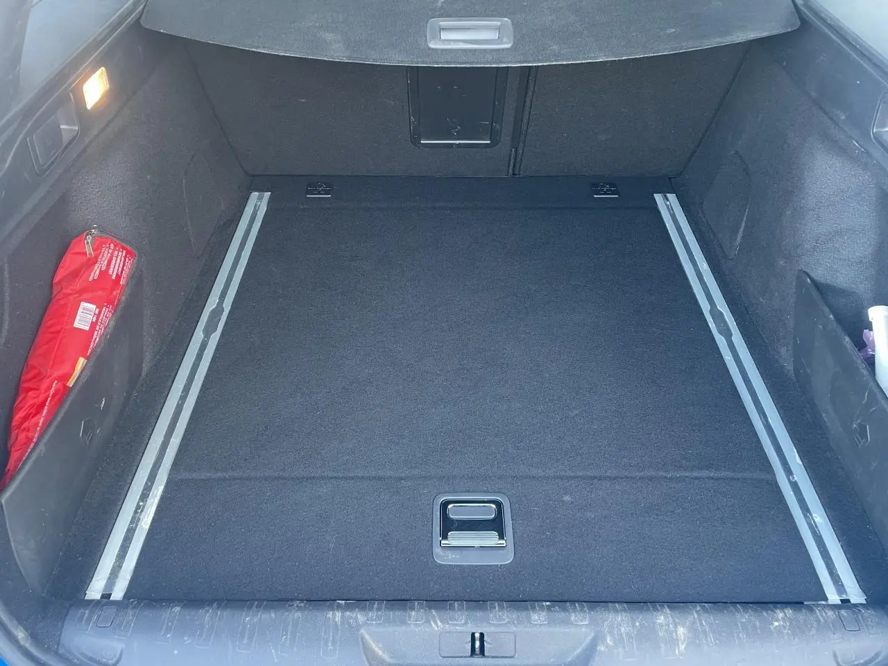 Coffre spacieux de Peugeot 308 SW 2 bleu Vertigo, vue intérieure avec rails de coffre et rangement latéral rouge.