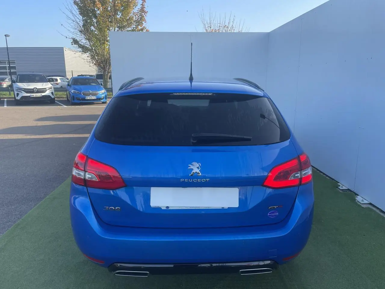 Vue arrière d'une Peugeot 308 SW bleu Vertigo avec double sortie d'échappement et vitres arrière surteintées.