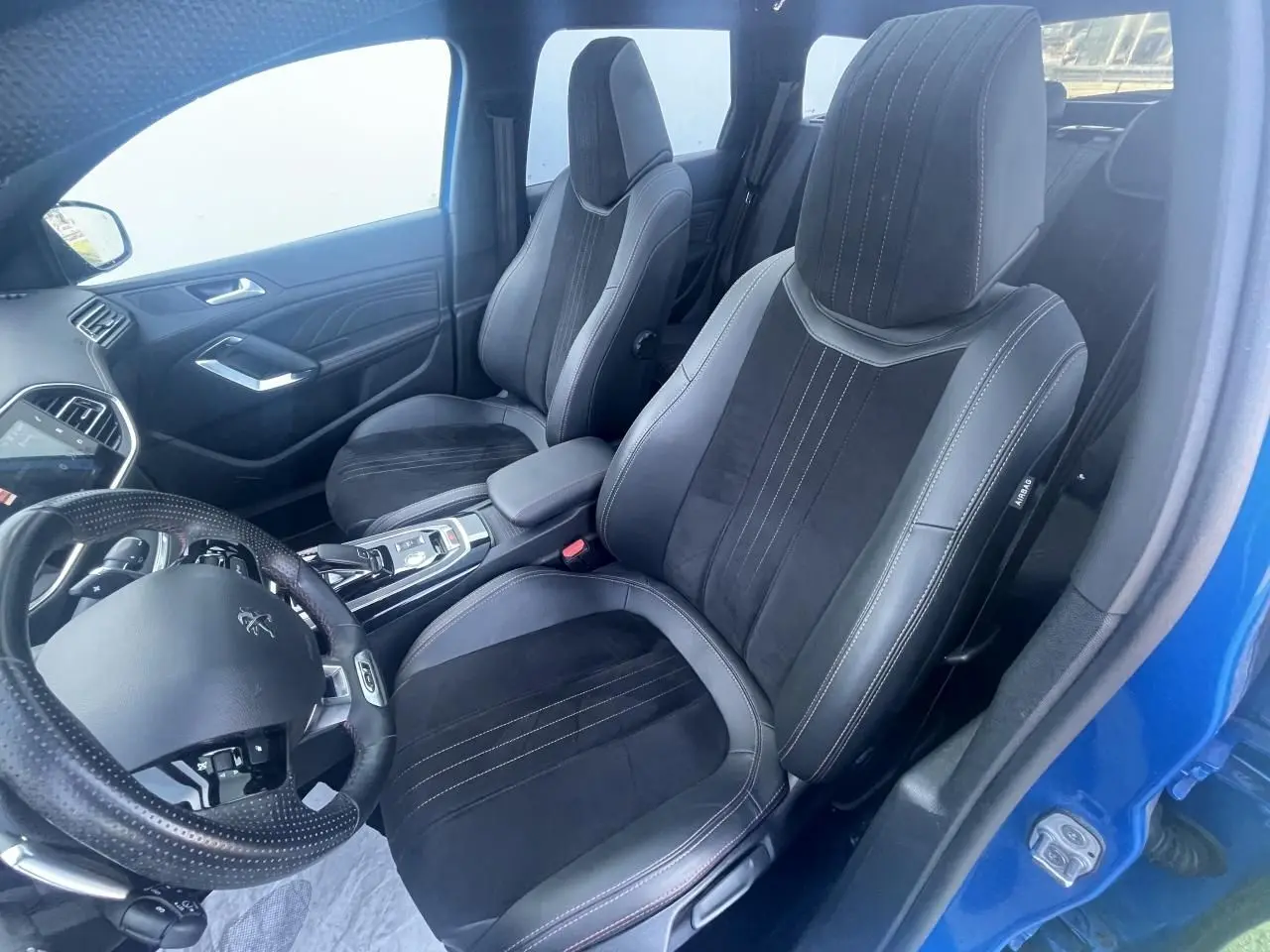 Vue intérieure côté conducteur d'une Peugeot 308 SW bleu Vertigo, sièges TEP et Alcantara noirs avec surpiqûres rouges.