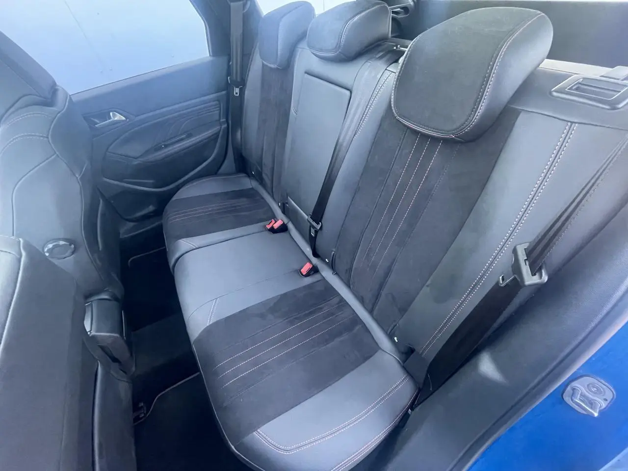 Vue intérieure côté arrière gauche montrant la banquette arrière noire avec surpiqûres rouges d'une Peugeot 308 SW Bleu Vertigo.