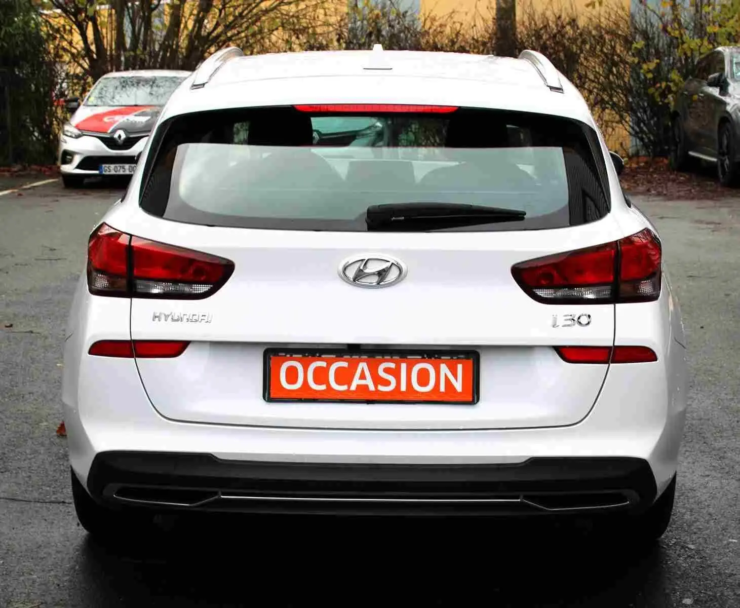 Vue arrière d'une Hyundai i30 SW blanche polaire avec plaque "OCCASION" en orange sur un parking extérieur.