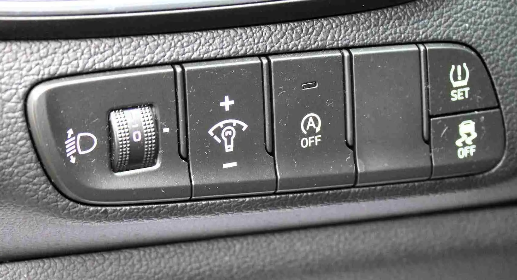 Gros plan sur les commandes de réglage d'éclairage, d'assistance et de sécurité du tableau de bord d'une Hyundai i30 SW blanche.