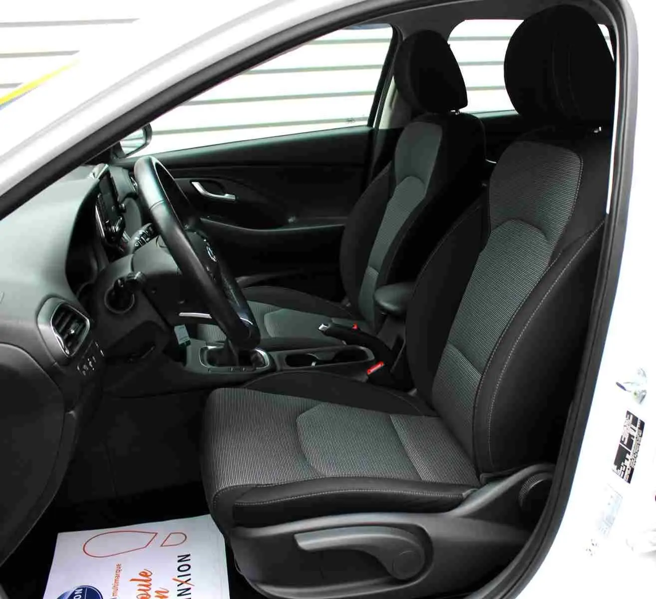Intérieur côté conducteur d'une Hyundai i30 SW blanc polaire 2022, sièges tissu gris et noir, volant et tableau de bord visibles.