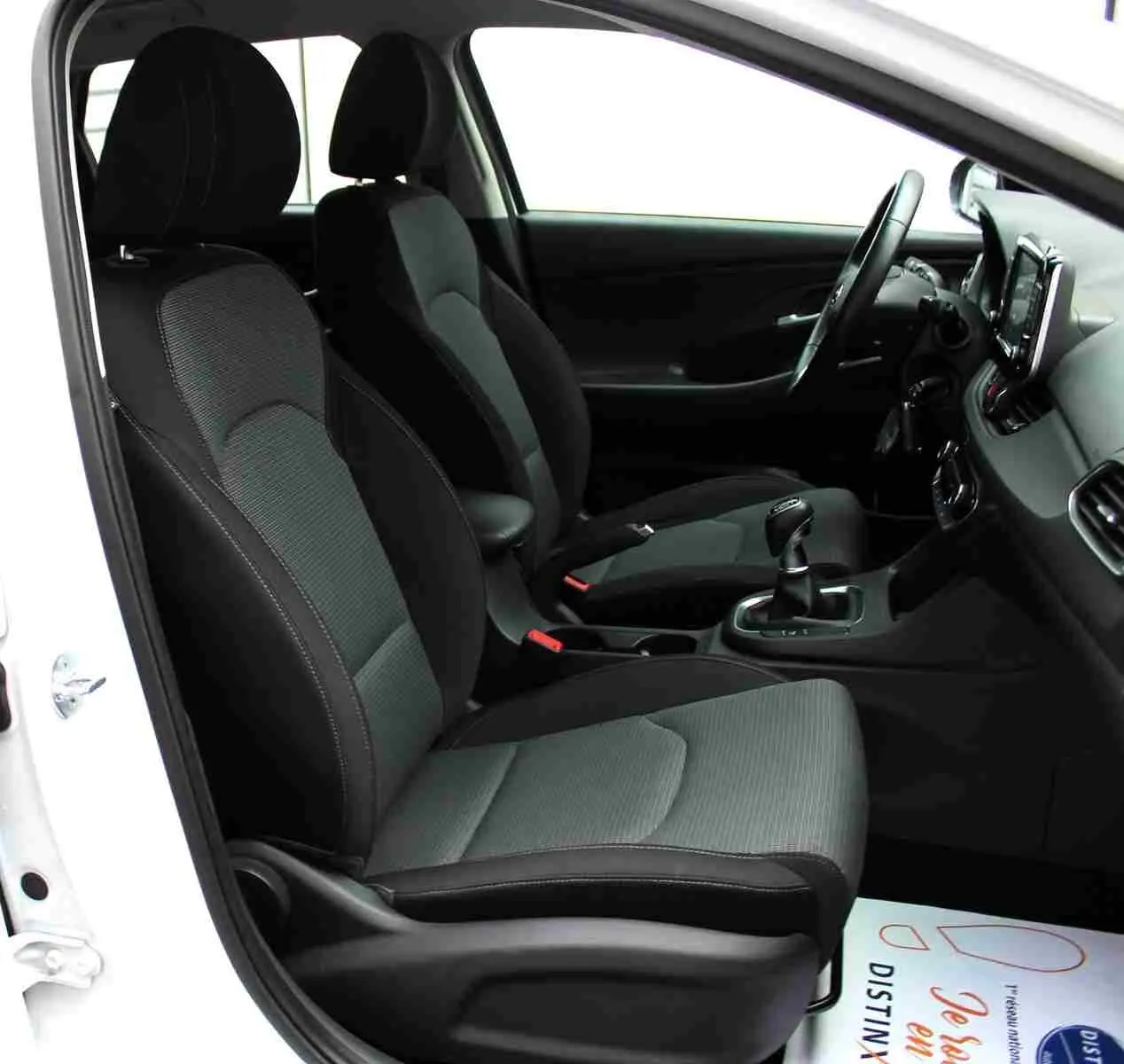 Vue intérieure côté conducteur de la Hyundai i30 SW 2022, sièges tissu gris noir et tableau de bord moderne.