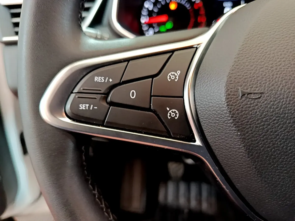 Gros plan sur les commandes de régulateur de vitesse au volant cuir noir de la Renault Clio Business TCe 100 blanche.