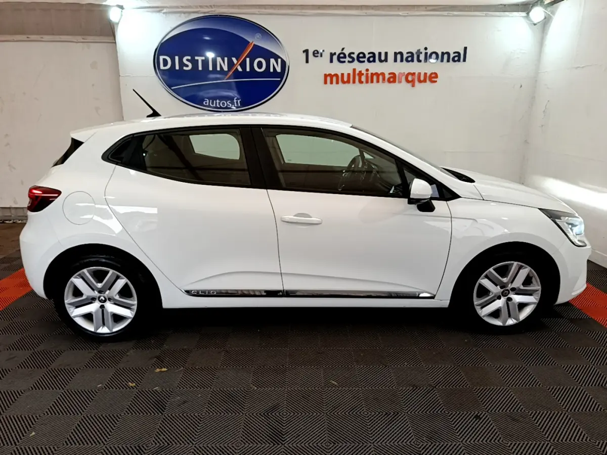 Profil côté gauche d'une Renault Clio Business TCe 100 blanche, avec jantes alliage et détails chromés sur les bas de porte.